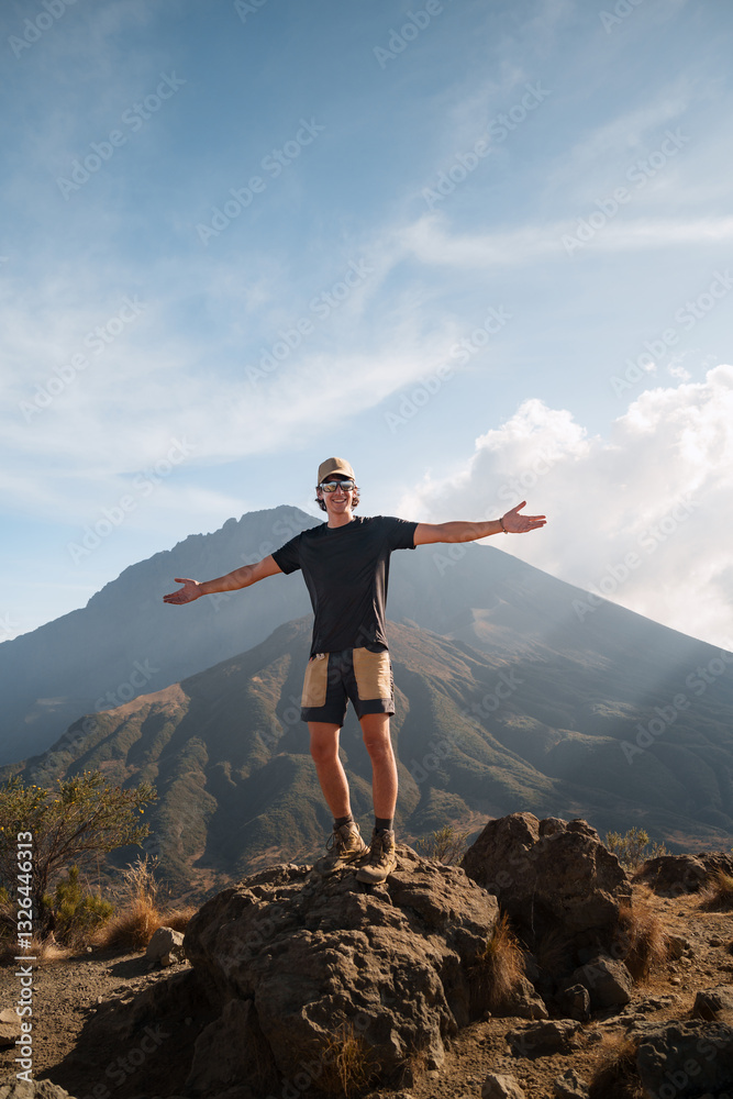 Tourist standing on mount meru summit with open arms enjoying the view. Backpacker standing on mount meru summit with open arms enjoying the breathtaking view, during a trekking experience in arusha n Tourist standing on mount meru summit with open arms enjoying the view. Backpacker standing on mount meru summit with open arms enjoying the breathtaking view, during a trekking experience in arusha n