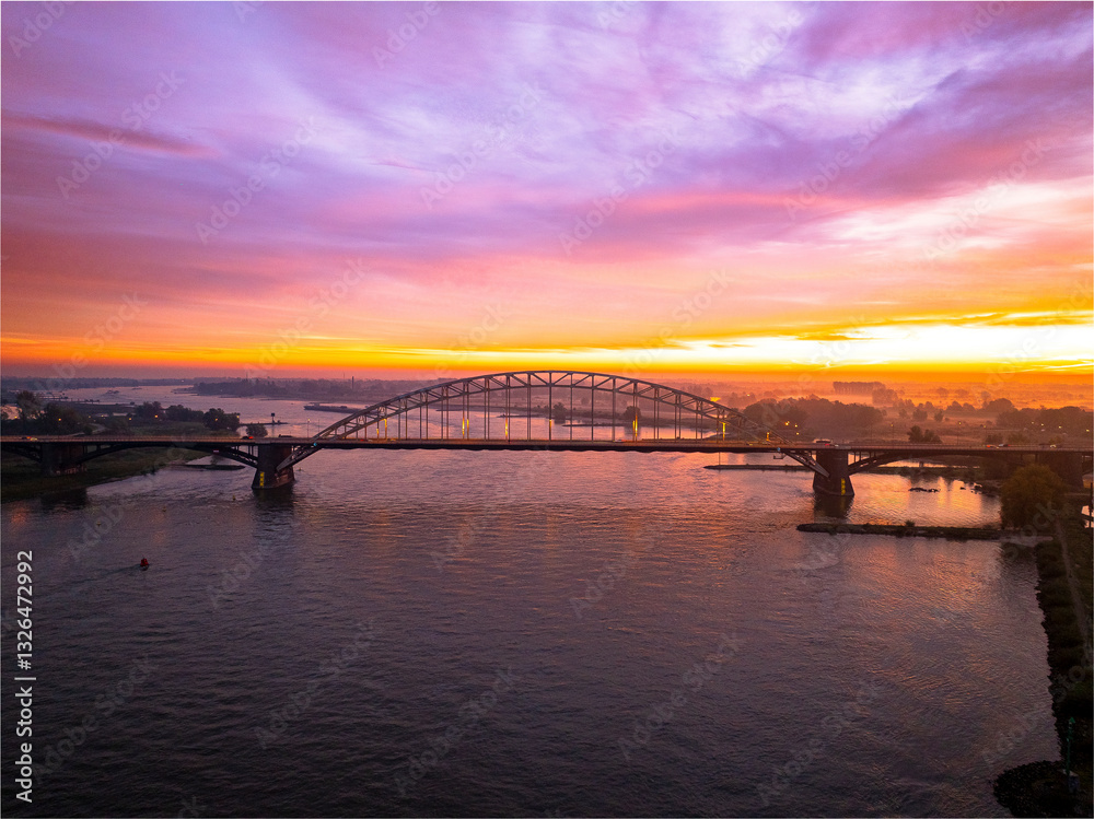 Aerial view of the beautiful Waalbrug bridge over the tranquil Waal river at sunset with a colorful sky, Nijmegen, Gelderland, The Netherlands. Aerial view of the beautiful Waalbrug bridge over the tranquil Waal river at sunset with a colorful sky, Nijmegen, Gelderland, The Netherlands.