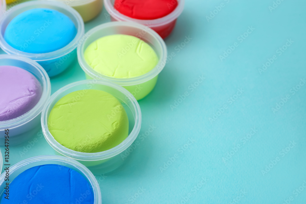Different colorful modeling clay in plastic jars on light blue background, closeup. Space for text Different colorful modeling clay in plastic jars on light blue background, closeup. Space for text