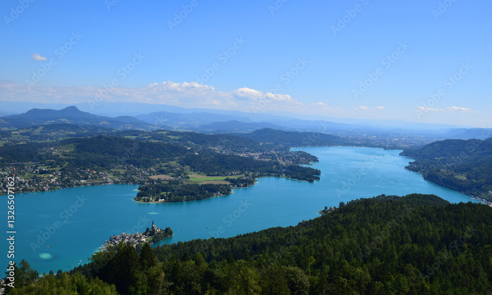 Aerial view of a historic village and church with a tall spire on the shores of Wörthersee, a stunning blue lake in the Austrian Alps. Green forests and mountains. European destination. Nature. Aerial view of a historic village and church with a tall spire on the shores of Wörthersee, a stunning blue lake in the Austrian Alps. Green forests and mountains. European destination. Nature.