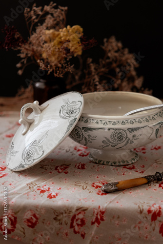фотографія Titre : Vintage soup tureen on floral tablecloth
Description : Elegant antique ceramic soup tureen with floral patterns, placed on a vintage tablecloth