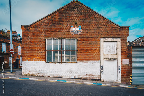 Abandoned Brick Building with Loyalist Symbol, Northern Ireland. Derry Londonderry. A red brick building in Northern Ireland, partially painted white at the base, featuring a loyalist emblem 