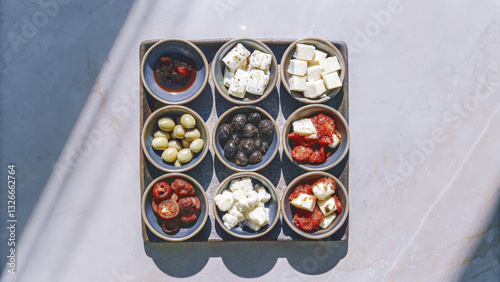 vibrant assortment of Mediterranean appetizers featuring olives, feta cheese, sun dried tomatoes, and herbs arranged in stylish tray. Perfect for sharing and enjoying with friends photo