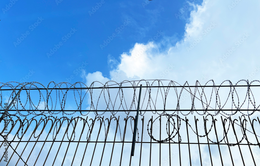 Razor wire or barbed tape, a mesh of metal strips with sharp edges, installed above iron bars fence, used to prevent trespassing of people. Razor wire or barbed tape, a mesh of metal strips with sharp edges, installed above iron bars fence, used to prevent trespassing of people.