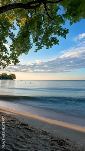 Serene beach scene at sunset with gentle waves, trees framing the shoreline, and clouds