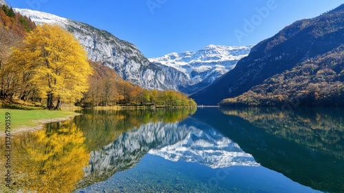 Autumnal landscape reflecting in a calm lake, surrounded by snow capped mountains under a vibrant blue sky. Golden and green trees line the lake's edge, creating a serene and picturesque scene.