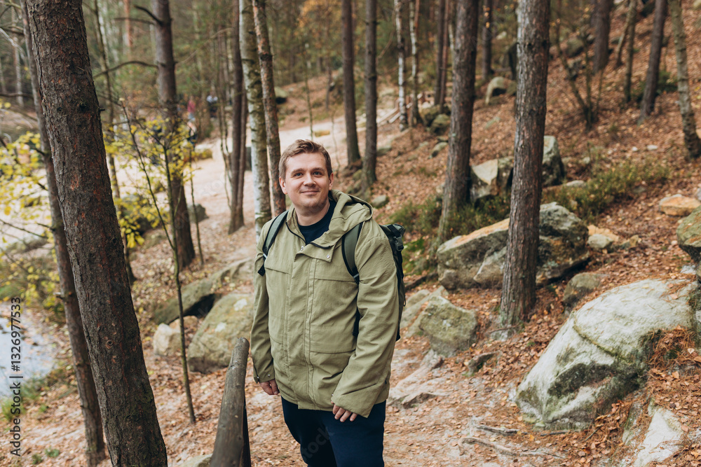 A tourist with a backpack stands against the background of a mountains and forest. Young 30s blonde man hiking in nature. Travel, adventure. Concept of an active lifestyle. High quality photo.