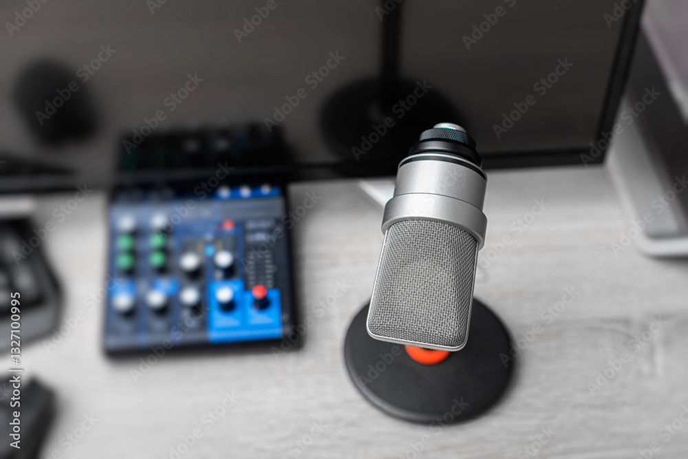 A professional condenser microphone on a desktop stand is set up in a modern gaming and recording workstation, surrounded by a computer monitor, keyboard, and gaming peripherals.