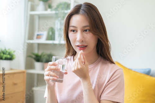 Dietary supplement, healthy diet positive asian young woman hand holding pill capsule, take vitamin in mouth for beauty skin hair, taking medicine with glass of water at home, pharmacy and health care