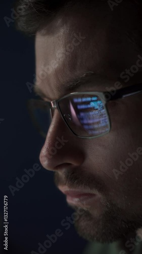 Close up of data scientist face is closely examines data. The glow of code lines reflecting in software engineer glasses and eyes. Vertical video