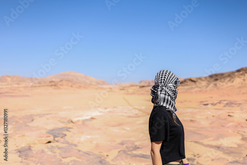 A person against the backdrop of a desert landscape with brown sand and hills.