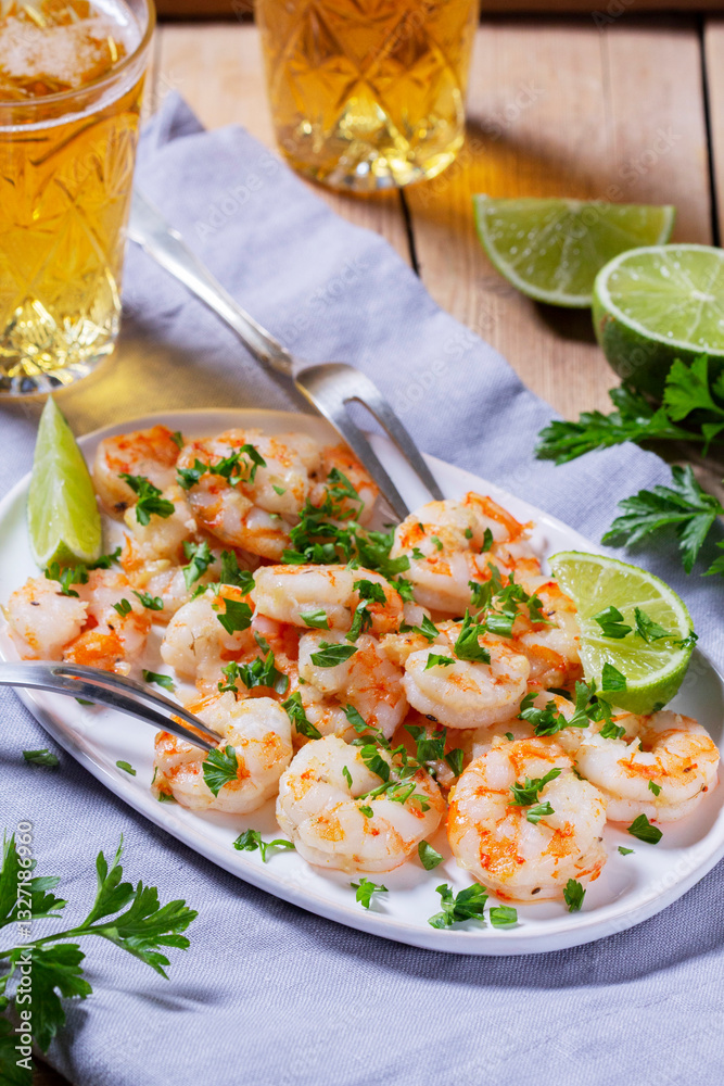 Shrimp cooked with garlic and herbs, served with beer and lime on a wooden table.