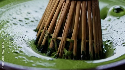 A close-up of a bamboo whisk stirring frothy green matcha tea, creating a smooth and vibrant texture, showcasing the traditional Japanese tea ceremony technique