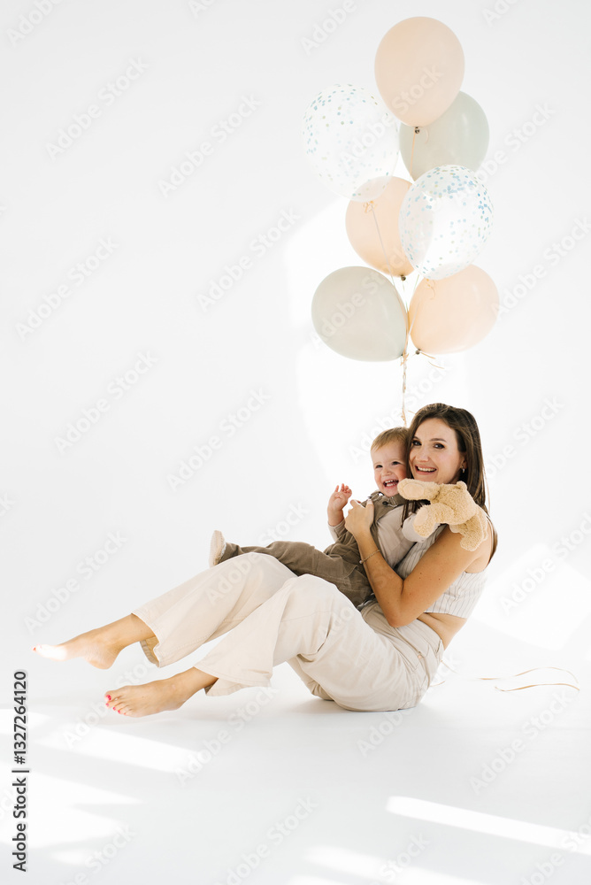 Young woman mother and child boy son are sitting on the floor, surrounded by birthday balloons