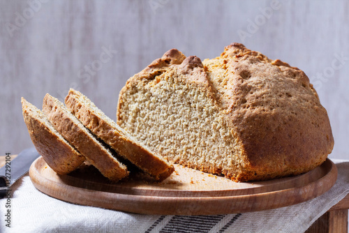 Homemade Irish soda bread cut into pieces and knife on wooden background.