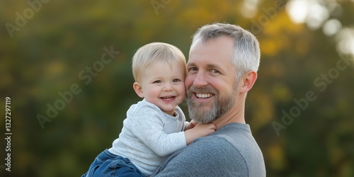 A man and a child are smiling and holding hands. The man is wearing a gray shirt and the child is wearing a white shirt. Scene is happy and warm