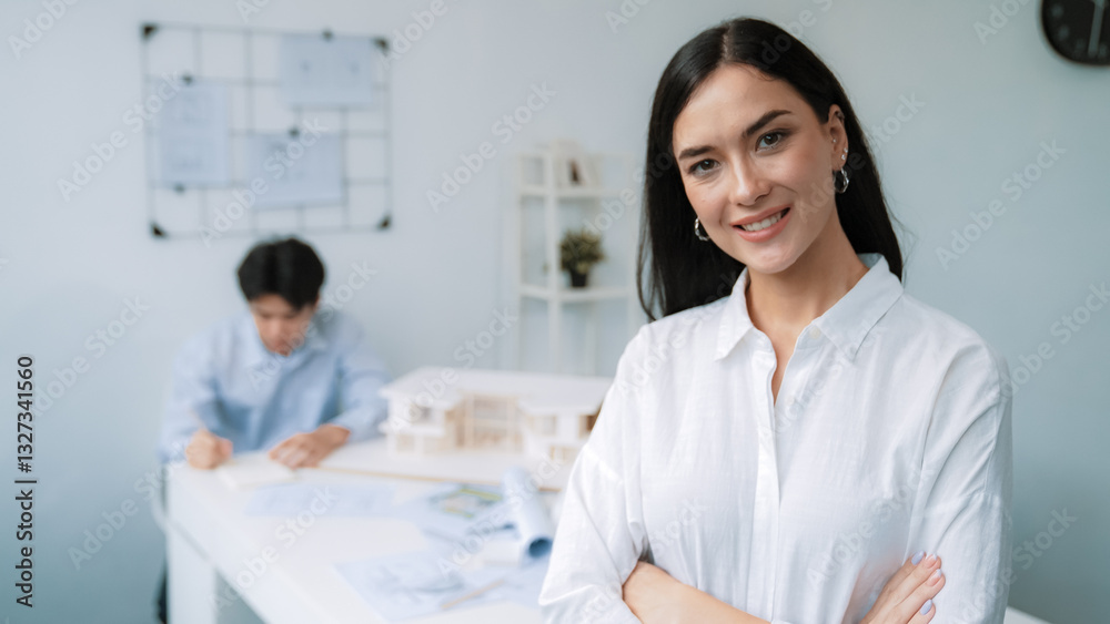 Closeup of female professional architect engineer cross arms with confident while skilled coworker focus on drawing blueprint at table with house model. Creative living and design concept. Immaculate. Closeup of female professional architect engineer cross arms with confident while skilled coworker focus on drawing blueprint at table with house model. Creative living and design concept. Immaculate.