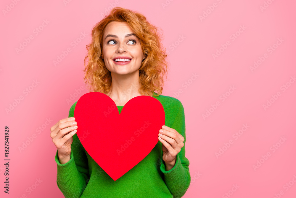 Smiling Young Woman Holding a Red Heart Shape Symbolizing Love Against a Pink Background, Wearing a Green Sweater Smiling Young Woman Holding a Red Heart Shape Symbolizing Love Against a Pink Background, Wearing a Green Sweater