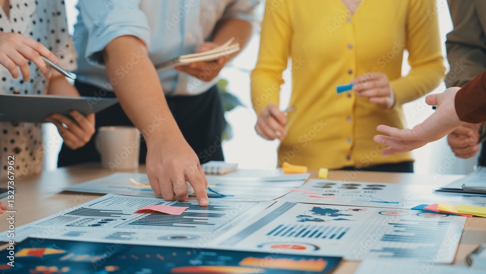 Fototapeta premium A dynamic group of professionals collaborates in a bright office space. They analyze various graphs and charts while discussing strategies using sticky notes and documents. SACTR