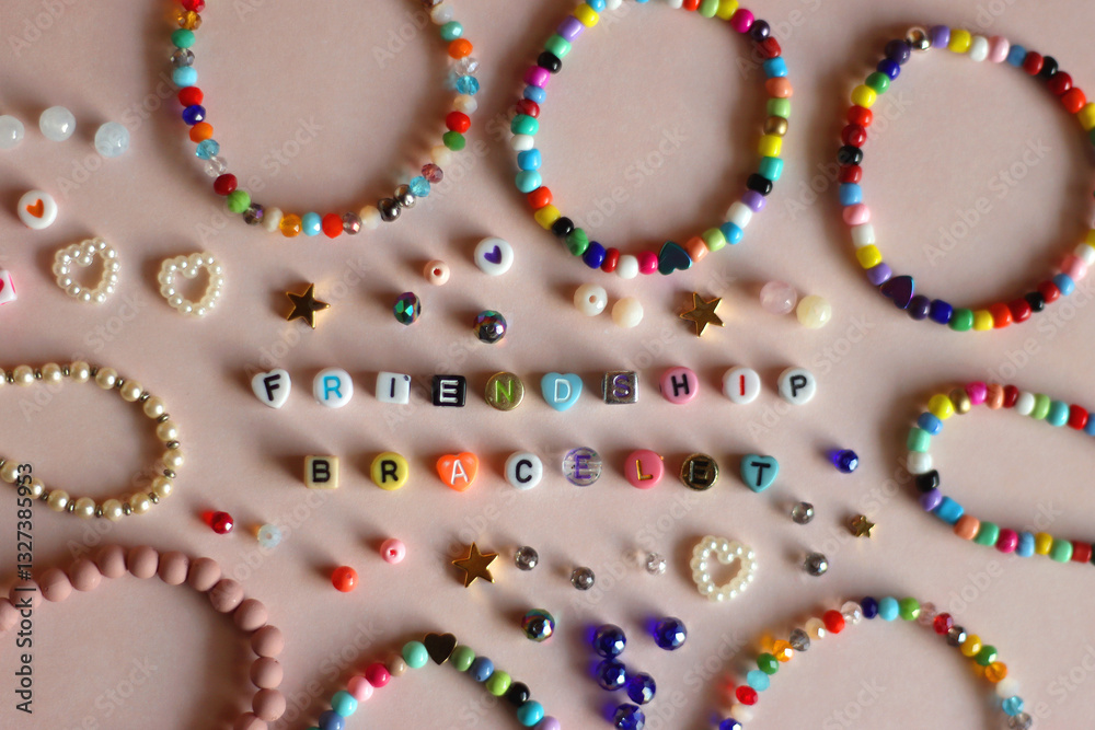 Friendship bracelet spelled with letter beads. Colorful handmade bracelets and various beads. Flat lay, pink background.