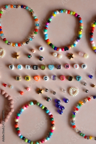 Obraz na płótnie Friendship bracelet spelled with letter beads. Colorful handmade bracelets and various beads. Flat lay, pink background. w salonie