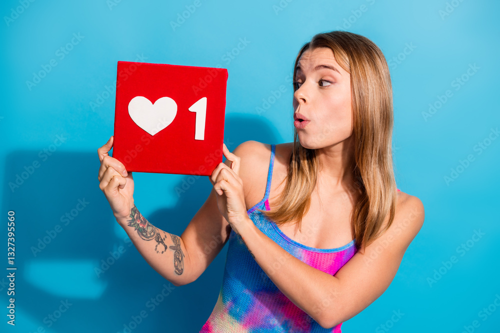 Young Woman Holding a Heart Symbol Sign with One Like Count Against a Vibrant Blue Background Displaying Excitement and Happiness Young Woman Holding a Heart Symbol Sign with One Like Count Against a Vibrant Blue Background Displaying Excitement and Happiness