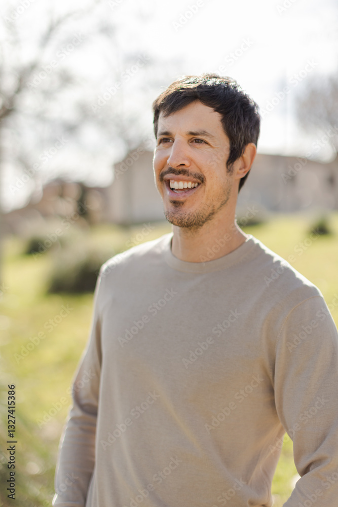 Cheerful middle-aged Caucasian man smiles while gazing into the distance, enjoying the moment. Warm sunlight enhances the peaceful outdoor. Vertical, soft-focus background with trees and building Cheerful middle-aged Caucasian man smiles while gazing into the distance, enjoying the moment. Warm sunlight enhances the peaceful outdoor. Vertical, soft-focus background with trees and building