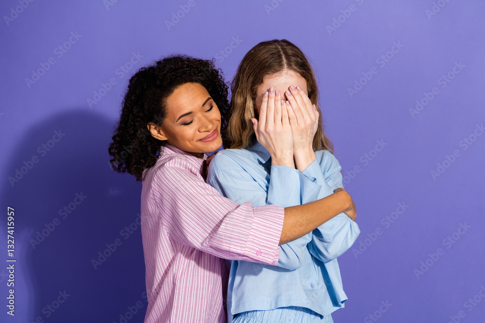 Two young women in stylish pajamas showing friendship and nurturing emotions against a vibrant purple background Two young women in stylish pajamas showing friendship and nurturing emotions against a vibrant purple background