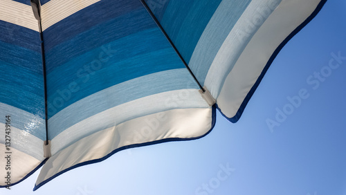 White and shades of blue striped beach umbrellas. View from below. Blue sky. Relaxing context. Summer holidays at the sea. General contest and location