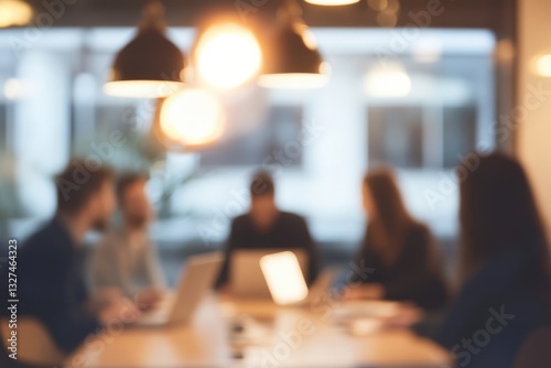 blurred photo of an office meeting room with business people sitting around the table with laptops and documents, discussing business plans, talking and working together