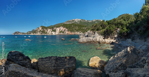 Obraz na płótnie Calm clear green sea near shore with large rocks, sun shines to small waves, boats at distance, typical scenery at one of many bays in Liapades, Greece w salonie