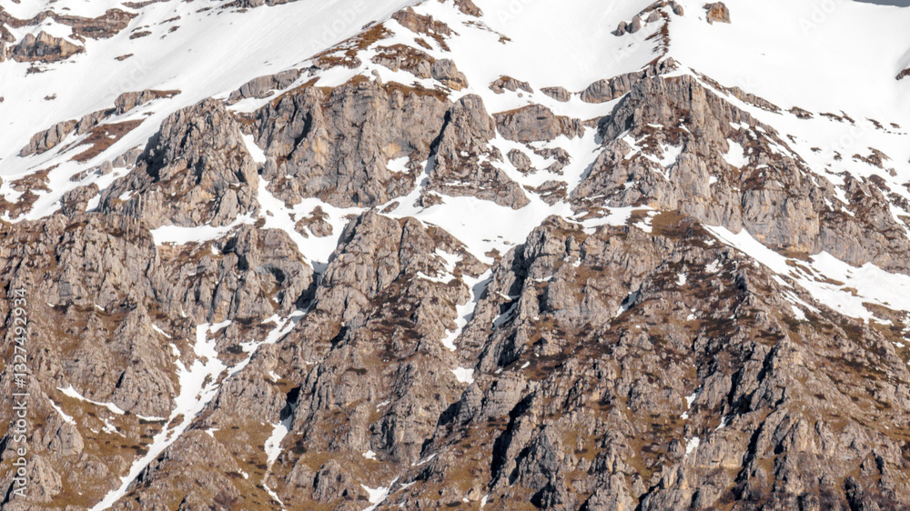 Aerial view of rocks on a mountain partly covered by snow. Ideal for textures, backgrounds and patterns.