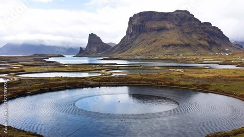 Nature's Canvas: A breathtaking landscape unfolds, revealing a serene lake with captivating circular patterns, framed by imposing mountains under a cloudy sky.