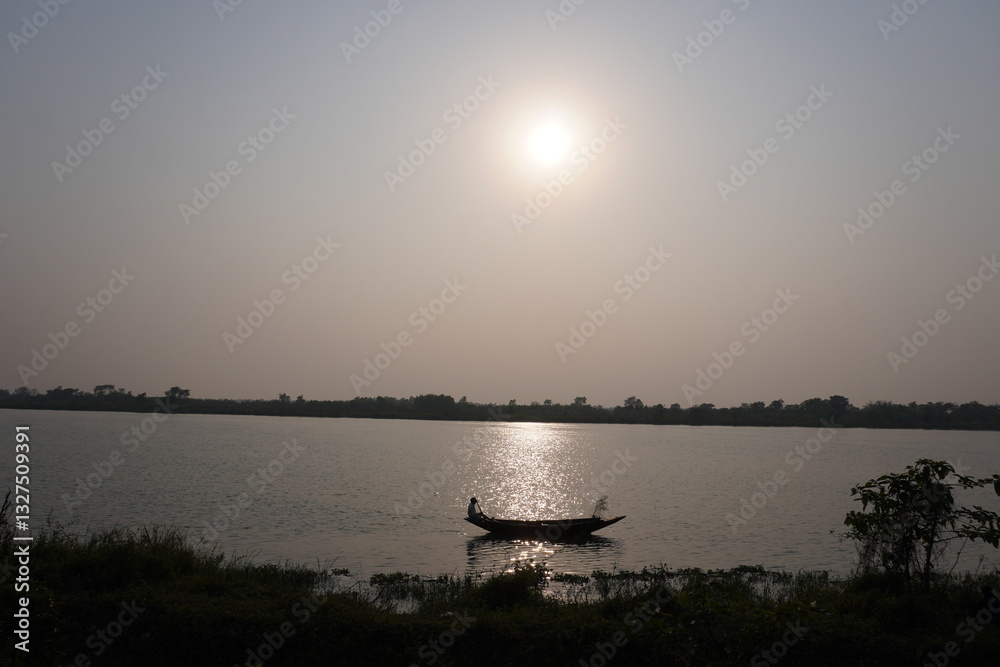 Naklejka premium A person is sailing a boat on the water near the river bank, sunset in the background