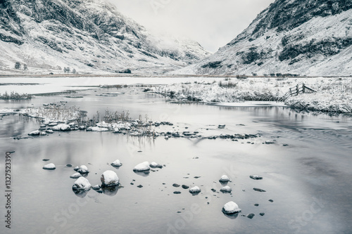 Loch Achtriochtan lake in Glencoe valley of Scottish highlands during overcast winter day with a couple of snow capped stones in foreground and mountains in background, winter atmosphere, Scotland.  photo