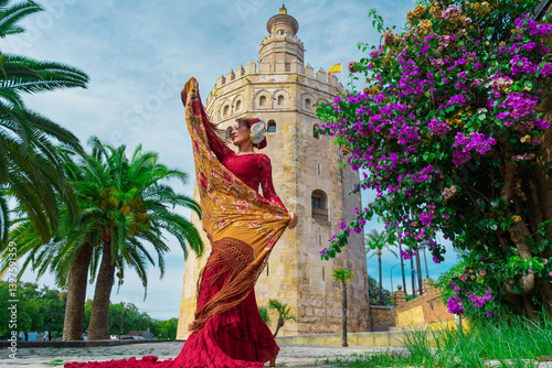 Mujer típica española bailando flamenco con una torre medieval y el cielo a su espalda. Desde la ciudad de Sevilla, Andalucía, España, Europa.	