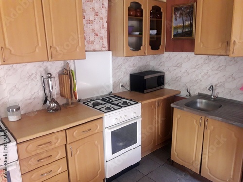 Fotografija A cozy kitchen with wooden cabinets, a white stove, microwave, and sink, adorned