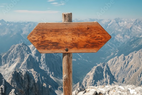 A weathered wooden sign points toward distant towering mountain peaks photo