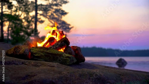 A cozy campfire burns on a rocky lakeshore during the white nights of summer solstice in Finland. Video with nature sounds for relaxation and meditation.