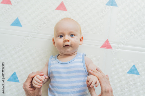 Obraz na płótnie A baby lies on a soft children play mat while their father hands gently support and protect them. Heartwarming moment of care and connection. Parenthood, safety, and love concept w salonie