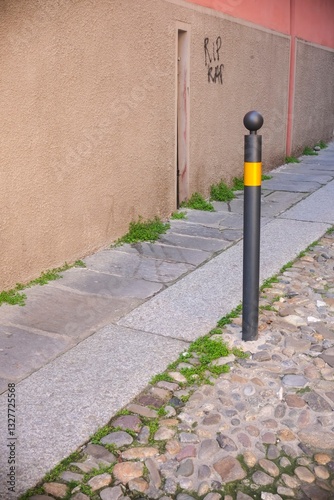 Black and yellow bollard separating sidewalk from cobblestone street in a typical italian urban setting