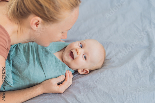 Obraz na płótnie A mother gently wraps her baby in a soft muslin swaddle, providing warmth and comfort. A tender moment of care and love between mother and child. Motherhood, baby care, and nurturing concept w salonie