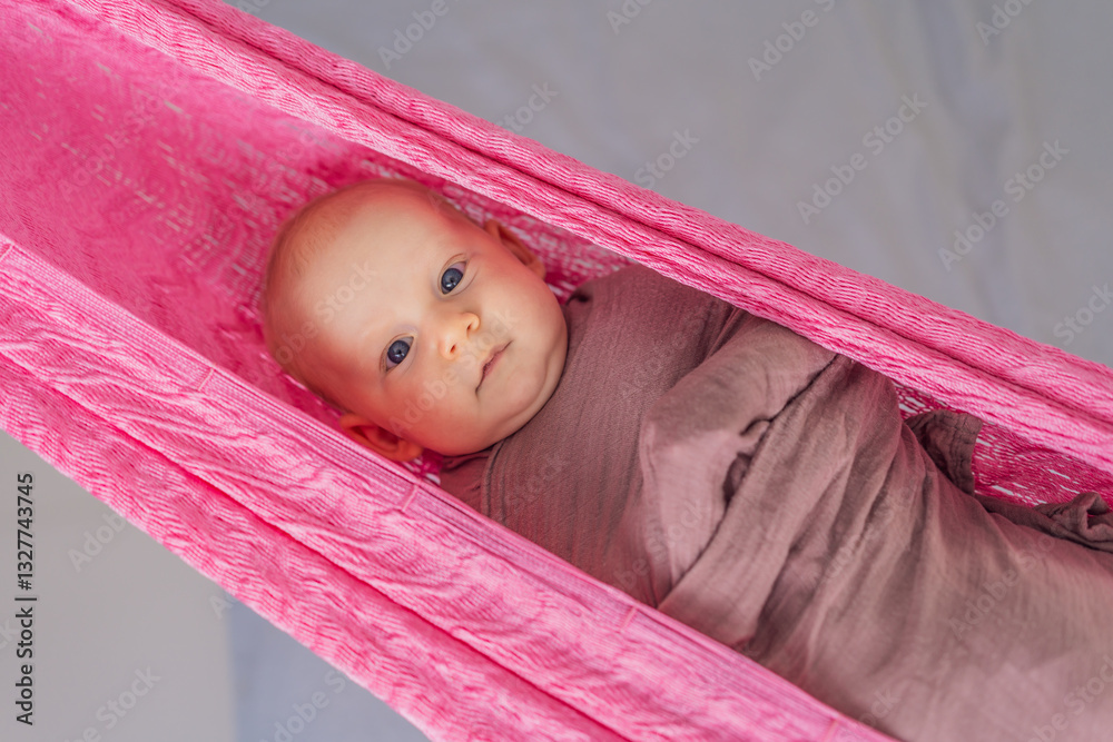 A 3-month-old baby peacefully falls asleep in a soft muslin swaddle while cradled in a cozy hammock. A serene and tender moment of comfort and relaxation. Baby care, rest, and tranquility concept