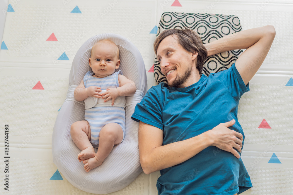 A loving father lies next to his 3-month-old baby, safely secured in a cozy infant cocoon with a special safety belt. Heartwarming family bonding moment. Parenthood, love, and baby care concept