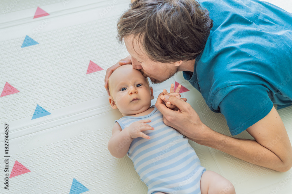 A baby lies on a soft children play mat while their father hands gently support and protect them. Heartwarming moment of care and connection. Parenthood, safety, and love concept