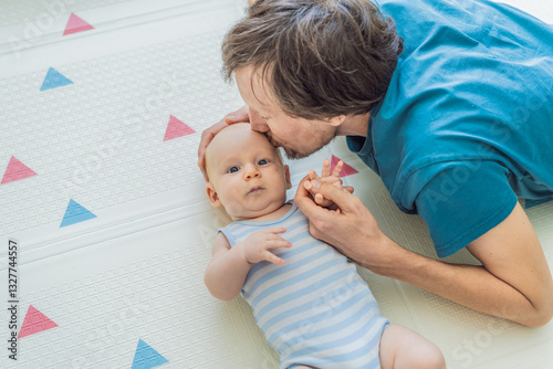 Obraz na płótnie A baby lies on a soft children play mat while their father hands gently support and protect them. Heartwarming moment of care and connection. Parenthood, safety, and love concept w salonie