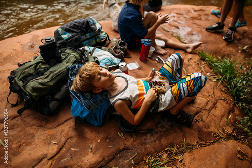 Boy laying on backpack in the woods having a snack