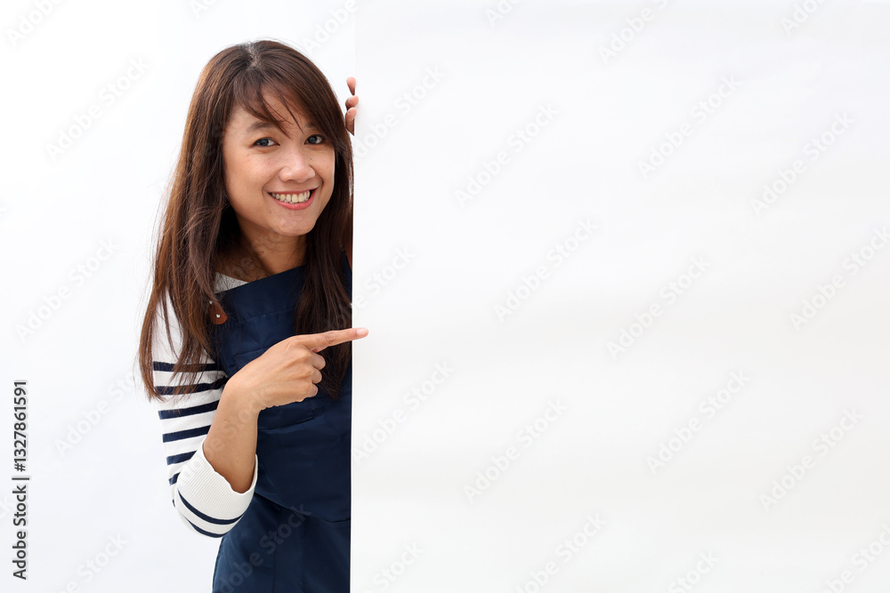 Cheerful Asian woman in apron pointing something on white advertisement board on white background Cheerful Asian woman in apron pointing something on white advertisement board on white background