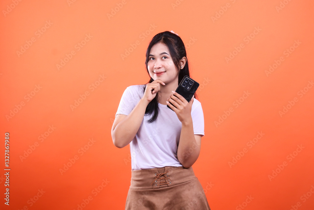 Obraz premium Woman in white shirt holding a mobile phone on orange background smiles at camera