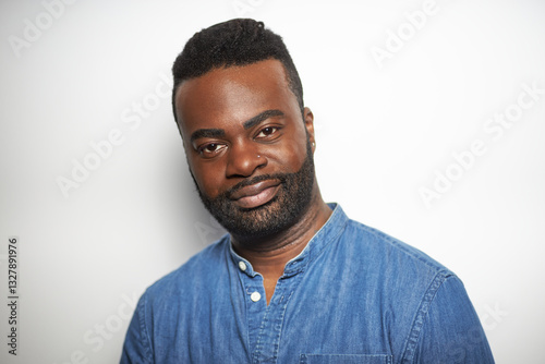 Portrait of a confident Black man with well-groomed beard wearing a denim shirt against a white background